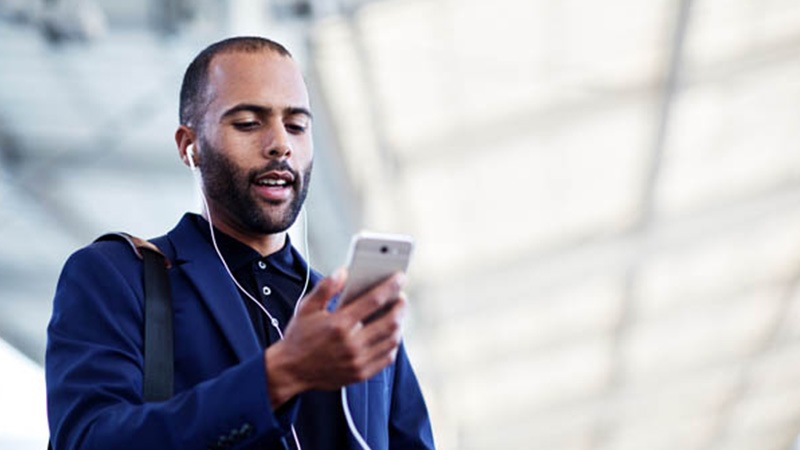 Man wearing earbuds and looking at a cell phone 