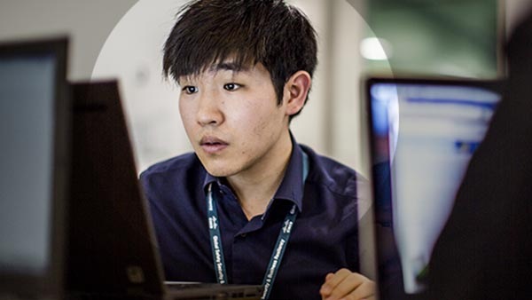 An Asian male employee working at his desk on his laptop.