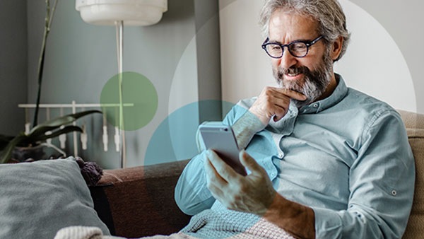 An older man with grey hair sitting on his sofa thinking over his phone at home.