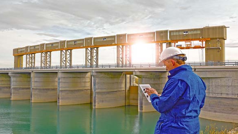 Man in hard hat standing at dam with tablet
