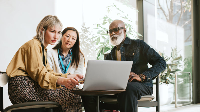 A group of three people collaborating around a laptop computer