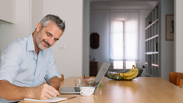 Man taking notes, in kitchen, using technology