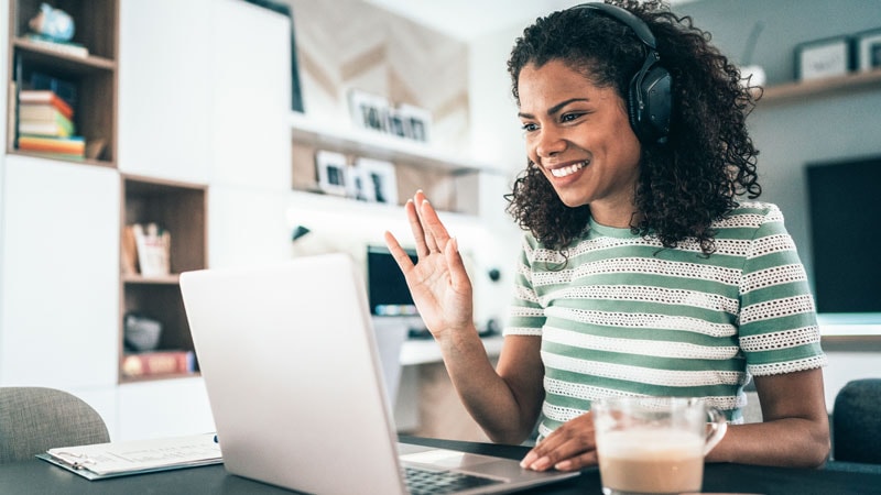 woman in home office, wearing headphones, waving at computer