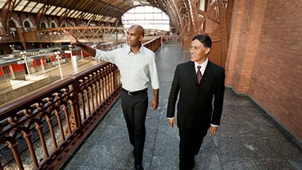 Two people walking on a mezzanine in a train station.