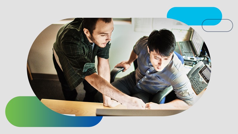 Two men at a desk looking at a screen together