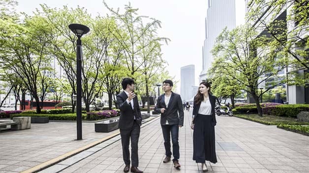 Three businesspeople talking and walking on a sidewalk.