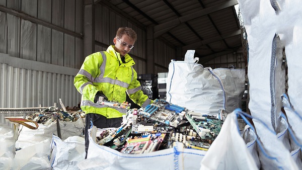 A worker wearing a neon yellow jacket, sorting e-waste