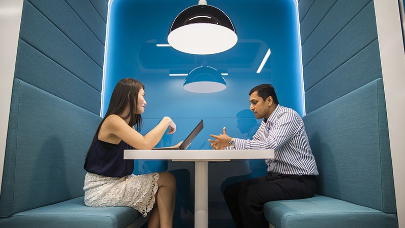 Individual on laptop sitting across another individual in a booth