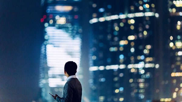 Panorama de ciudad nocturna con hombre usando un iphone
