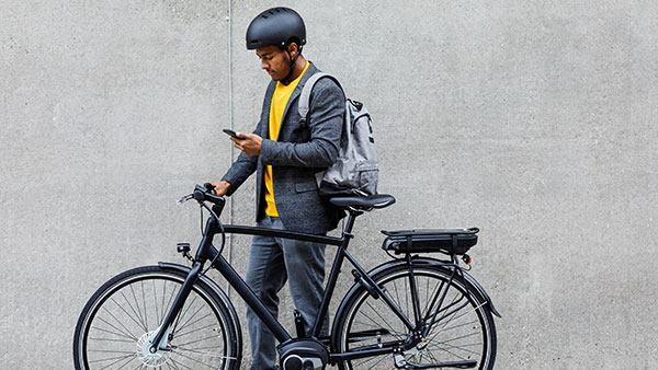 Un uomo fermo in piedi di fianco a una biciletta che guarda un iPhone