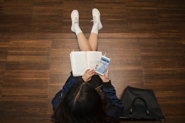 A student checking her cell phone while reading a book