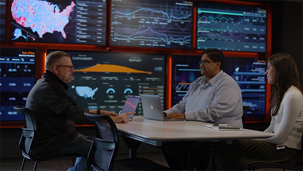 Three people sitting across screens with dashboards