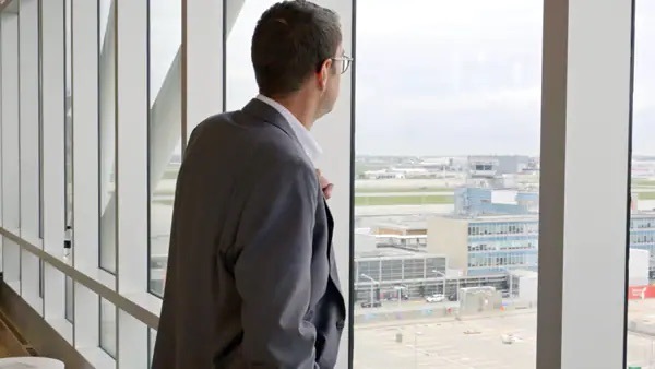 Man in suit looking out large window at Aéroports de Montréal