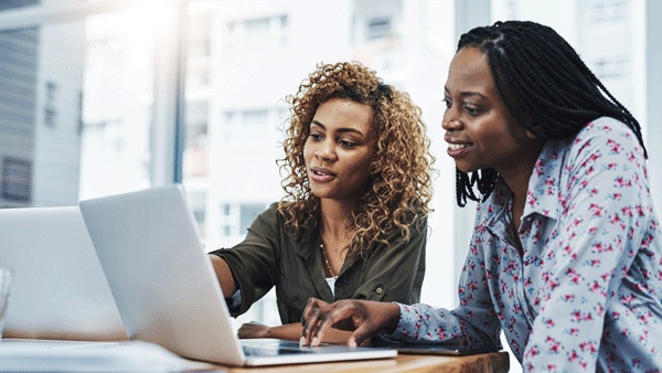 Two women talking while looking at their laptops 