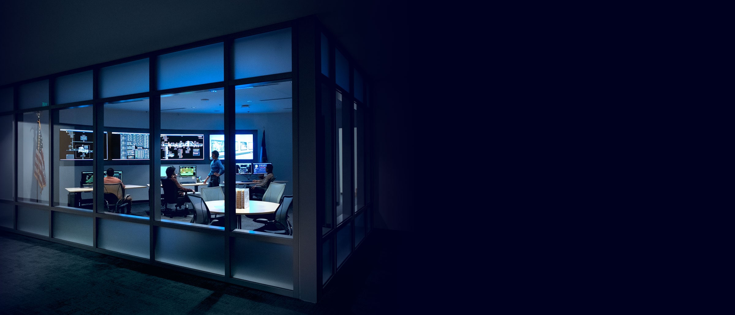 Federal employees in a glass room with TV monitors and computers