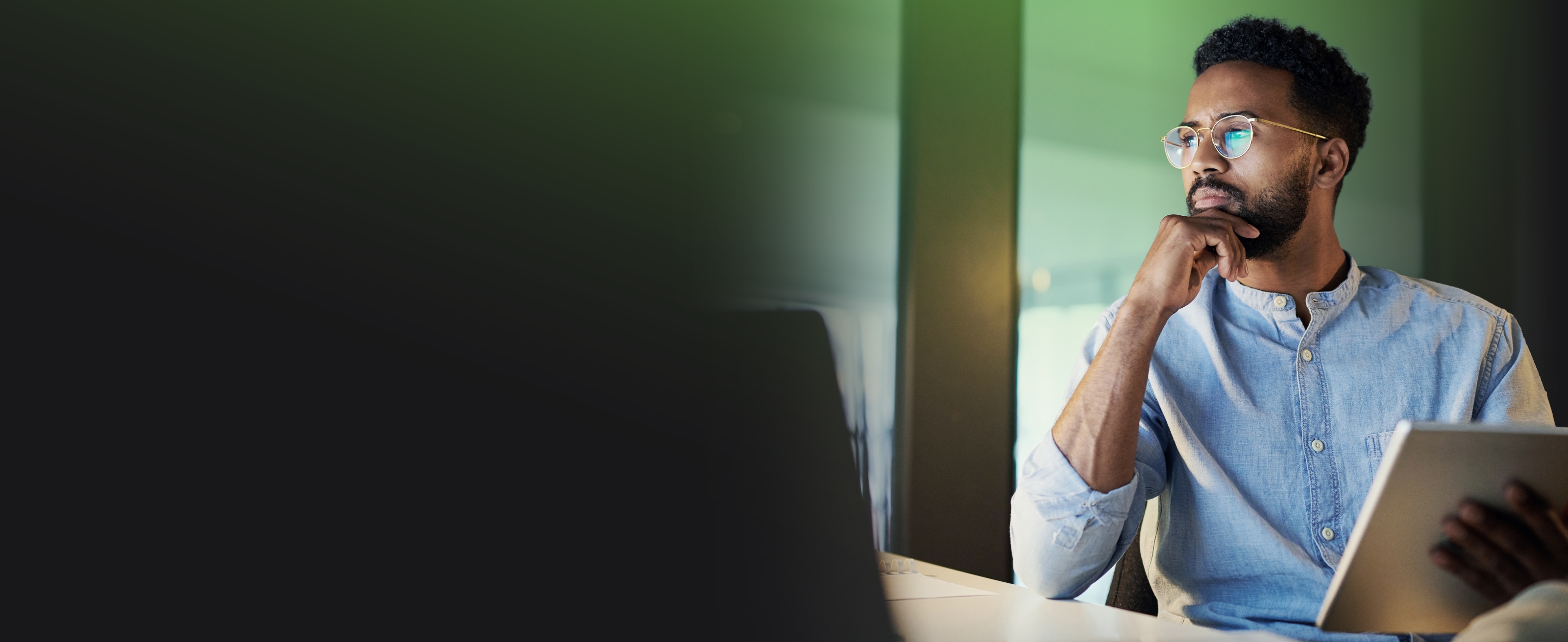 Homme avec des lunettes assis à un bureau et tenant une tablette