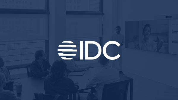 IDC logo over an in-office hybrid workplace photo featuring a conference table with workers viewing a Webex video conference on a large screen.