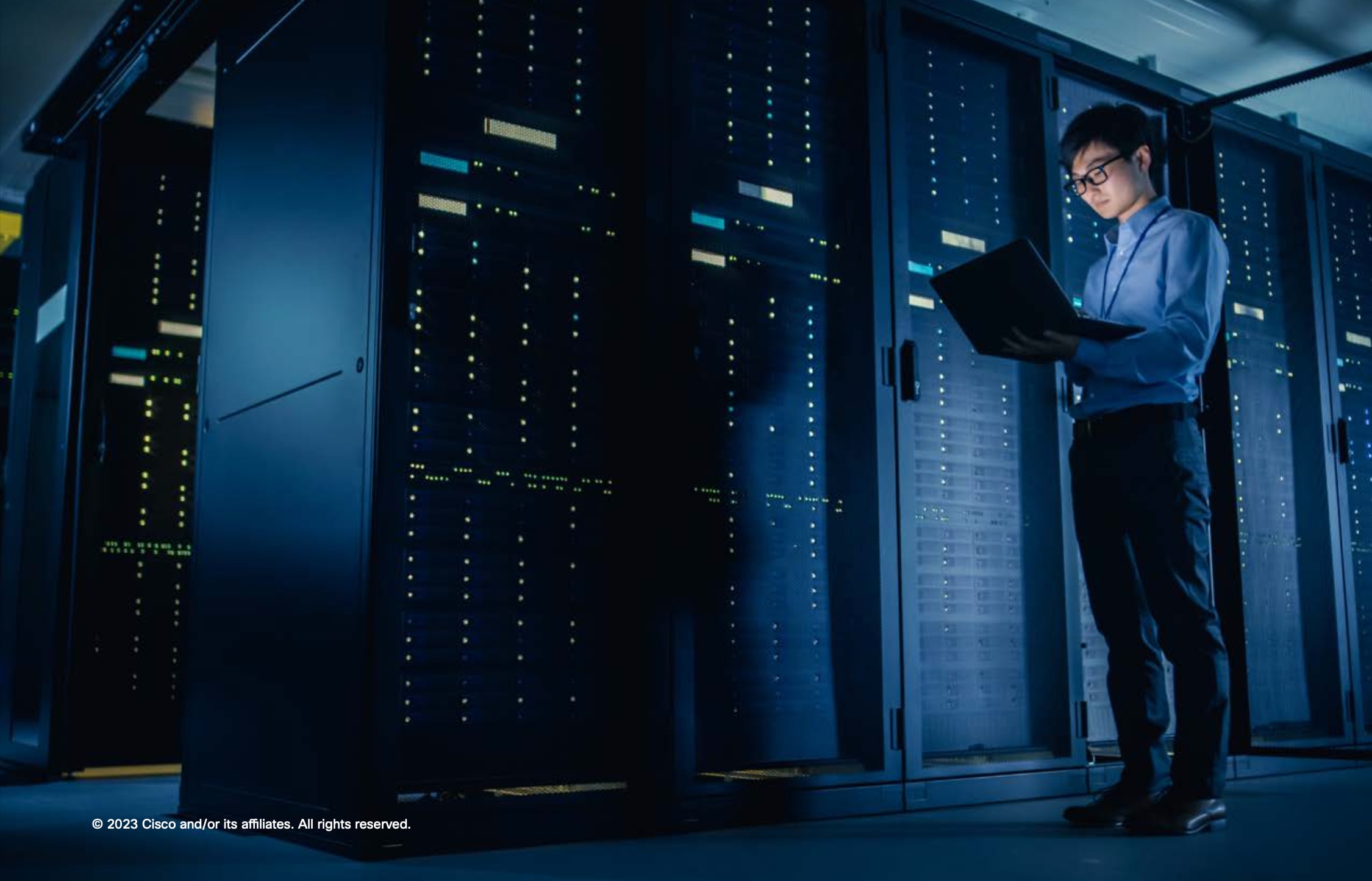 Man with open laptop standing next to data center or rows of server closets