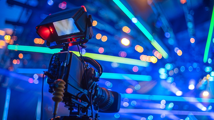 A professional video camera on a tripod, focused on a stage