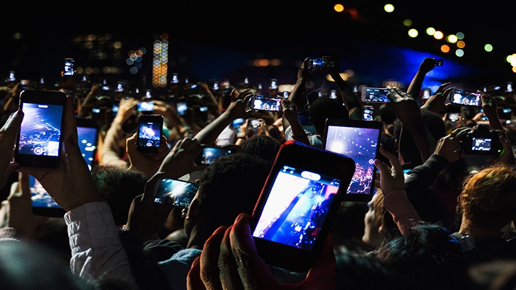 A crowd of people at a concert holding up smartphones to record the performance