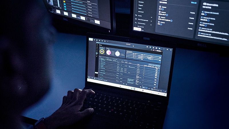 A person uses a laptop displaying security analytics dashboards.