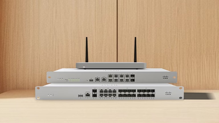 Stack of three Cisco networking appliances, including two rack-mount switches and a wireless gateway with antennas, on a wooden surface.