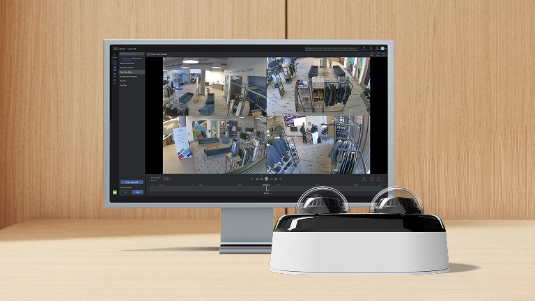 Cisco Meraki dashboard on a computer monitor showing four security camera feeds from a retail store, with two dome cameras in the foreground.