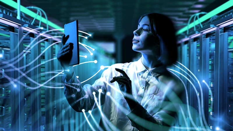 A person using a tablet in a server room, visualized with glowing blue data connectivity lines.