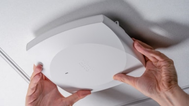 Two hands mounting a Cisco Wi-Fi 7 access point on the ceiling.